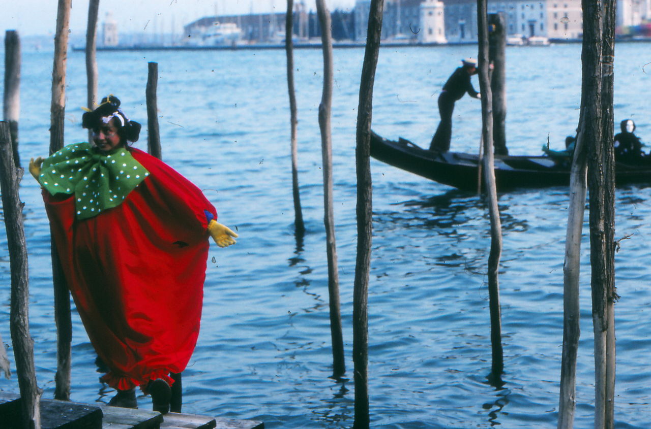 water, nautical vessel, nature, day, rear view, transportation, one person, full length, gondola, outdoors, boat, standing, clothing, boating, sea, men, mode of transportation, traditional clothing, travel destinations, travel, architecture, red, person, vehicle