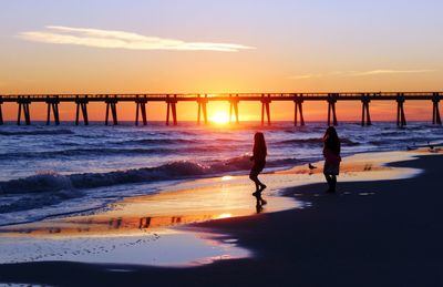 Silhouette women on beach against sky during sunset