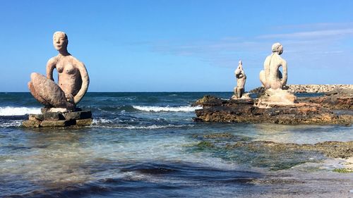 Statues on rocks in sea against sky