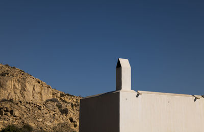 White building with chimney against mountain and blue sky