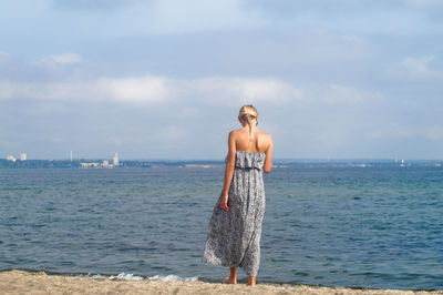 Full length of young woman standing on shore against sky