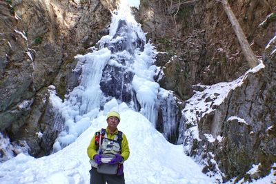 Man standing on snow covered land against rock formation