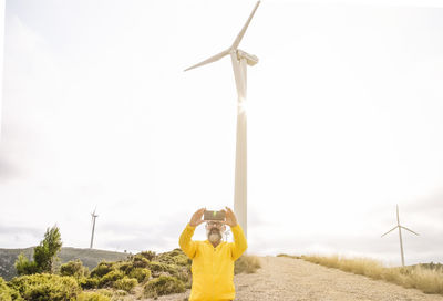 Man taking selfie near wind turbines at sunset