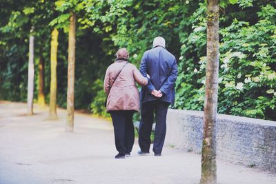 Full length rear view of couple walking in sidewalk by trees