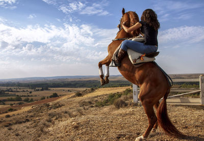 Woman riding horse on land against sky