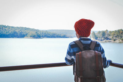 Rear view of boy with backpack standing by railing against lake