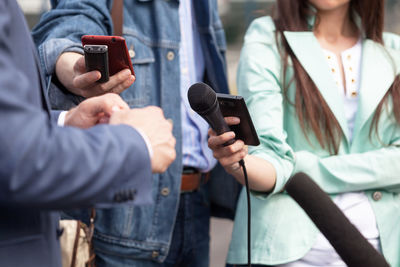 Midsection of people holding mobile phones and microphone