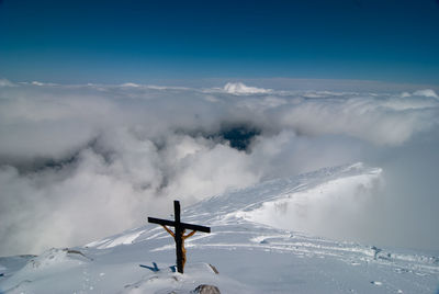 Low angle view of cross on snow covered landscape against sky