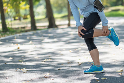 Low section of woman touching ankle and knee in pain on road