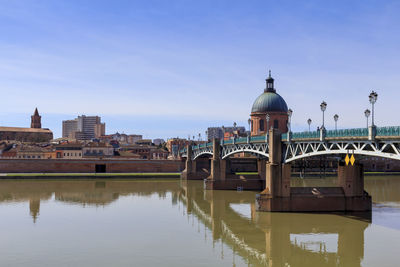 Bridge over river by buildings against sky in city