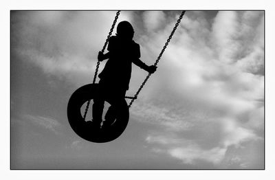 Silhouette boy swinging on tire swing against sky