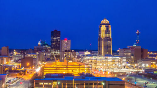 Illuminated buildings in city against blue sky