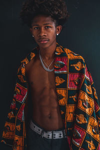 Portrait of young man standing with shawl against black background