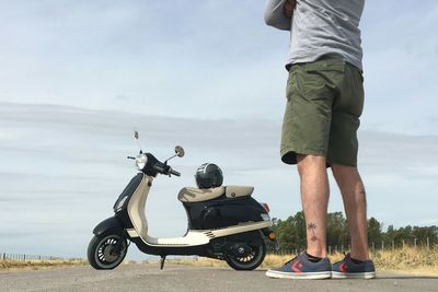 Low section of man standing on motorcycle against sky