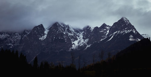 Silhouette trees on snowcapped mountains against sky