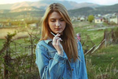 Beautiful young woman smoking while standing on field