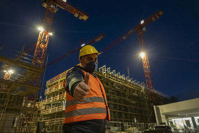 Construction worker posing at night wearing safety vest, hardhat and medical mask