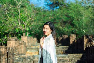 Smiling woman looking away while standing against trees