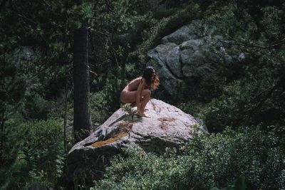 High angel view of naked woman on rock in forest