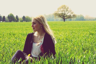 Portrait of young woman sitting on field against clear sky