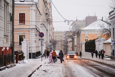 People walking on street amidst buildings in city during winter