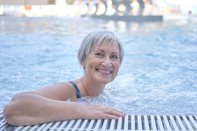 Happy senior woman with gray hair looking at camera in outdoor thermal pool with hydromassage. 