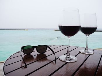 Glasses on table by sea against sky
