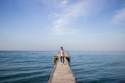 Man walking on pier over sea against sky