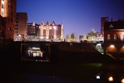 Illuminated buildings by river against sky at night