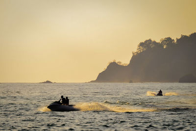 People on boat in sea against sky during sunset