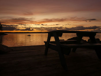 Silhouette table by sea against sky during sunset