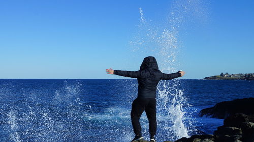 Man with arms outstretched standing against sea