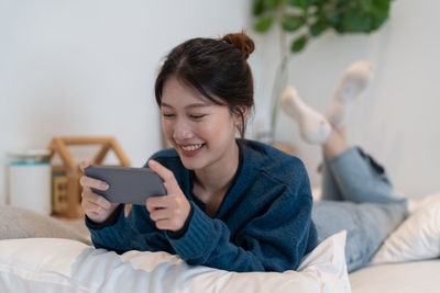Woman using smart phone lying on bed