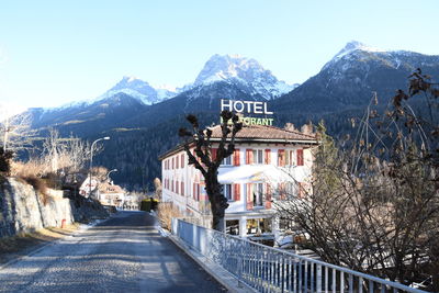 Road leading towards houses and mountains against clear sky