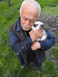 High angle view of senior man holding rabbit on grassy field