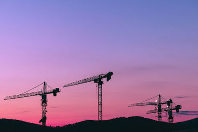 Silhouette cranes at construction site against sky during sunset