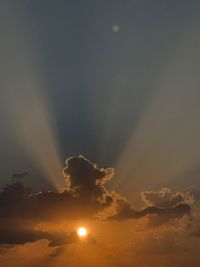 Low angle view of sun streaming through clouds during sunset
