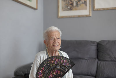 Smiling woman holding folding fan while sitting at home