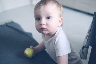 Cute one-year-old baby with apple in living room, toddler child eats apple in peel