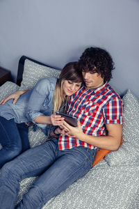 Couple using digital tablet while sitting on bed at home