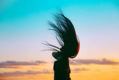 Woman tossing hair against sky during sunset