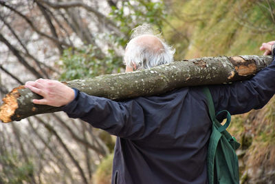 Rear view of man holding log while standing in forest