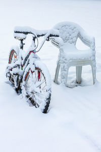 Snow covered bicycle by some chairs in winter