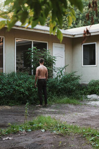 Rear view of shirtless man standing at back yard