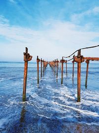 Wooden posts on pier over sea against blue sky