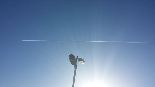 Low angle view of street light against vapor trail in clear blue sky