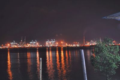 Illuminated cityscape by sea against sky at night