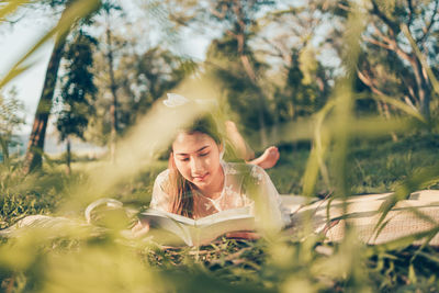 Portrait of young woman reading book on field