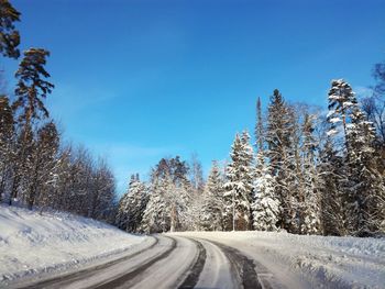 Road amidst snow covered trees against blue sky