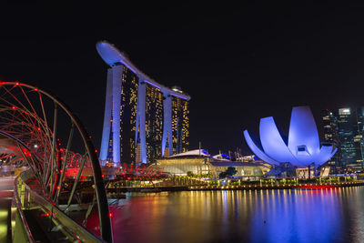 Illuminated marina bay sands in city by bay against clear sky